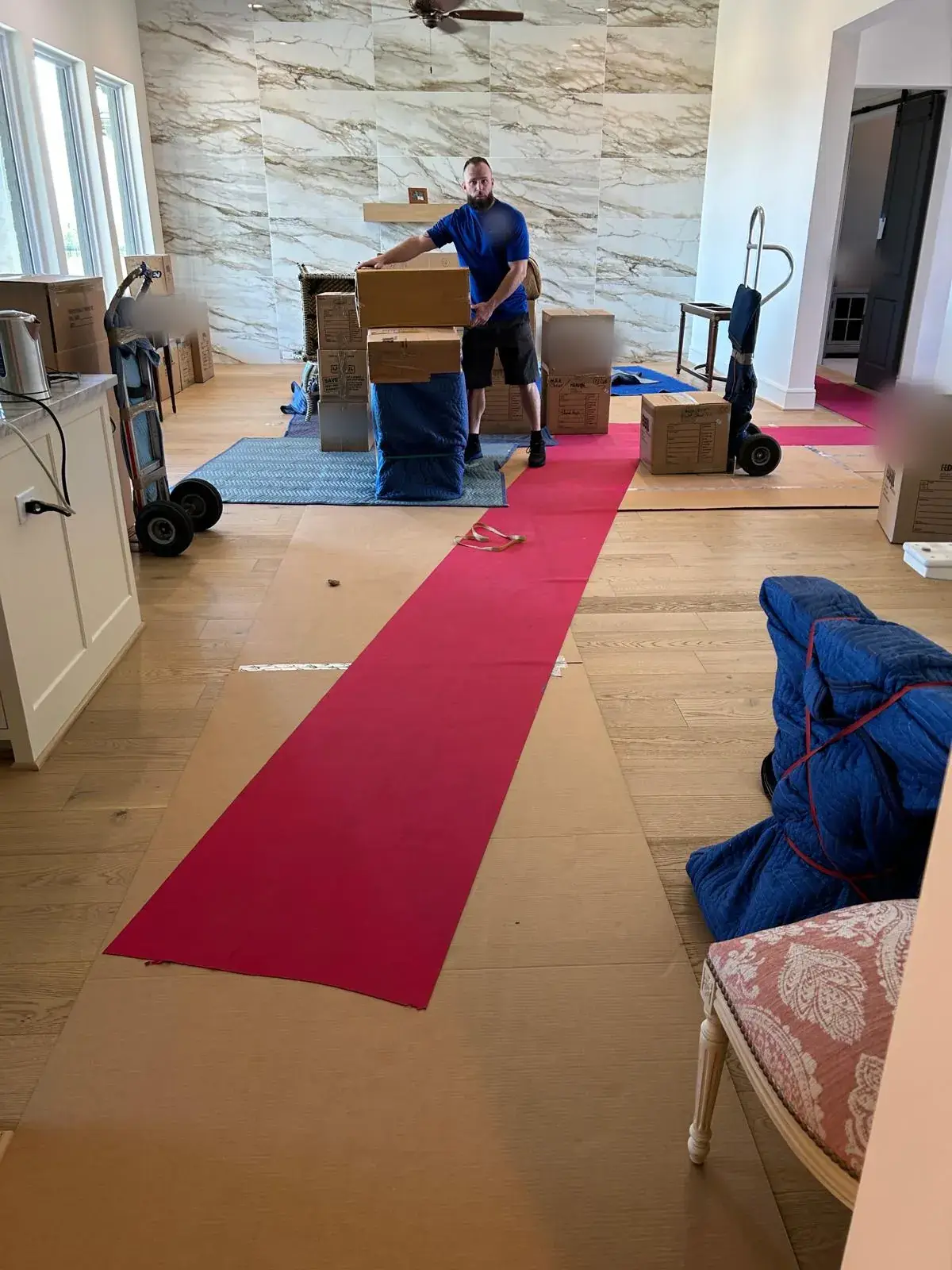 Champion Moving crew member with boxes, floor runners and padded furniture in a home