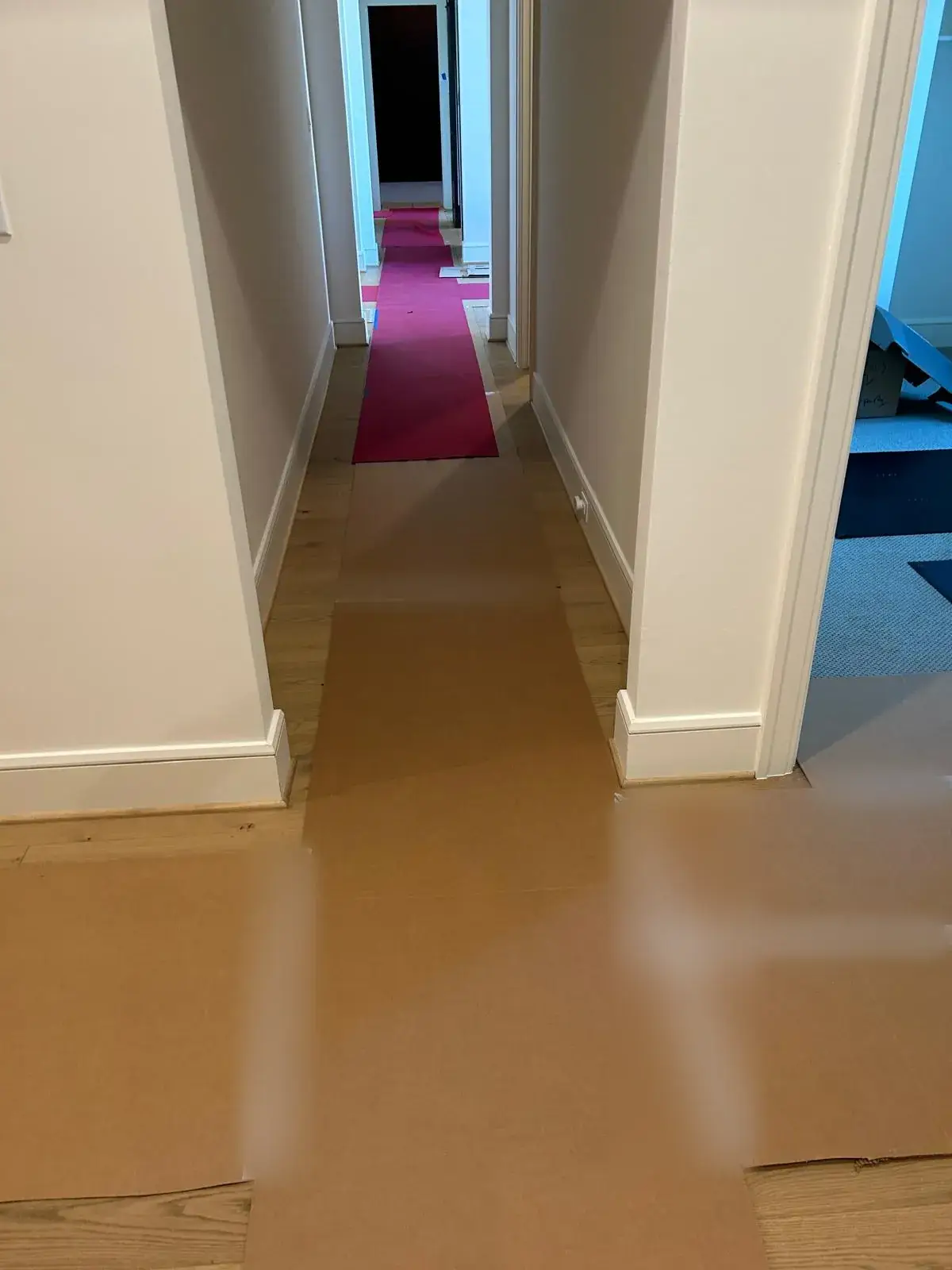 Hallway floors covered with protective board and a red runner during a move