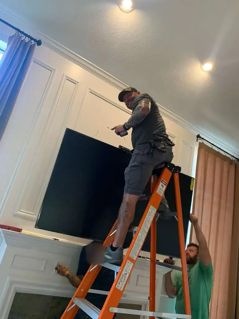 Champion Moving crew mounting a large TV above a fireplace from a ladder